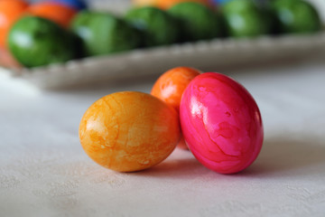 Fototapeta na wymiar Colorful and joyful Easter decorations on a table. Closeup color image of multiple painted Easter eggs with happy and vibrant colors including blue, green, orange, yellow and pink. Shiny marbled color