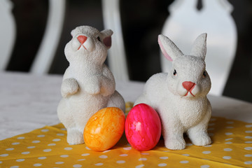 Colorful and joyful Easter decorations on a table. Closeup color image of two ceramic Easter bunnies and colorful painted Easter eggs with shiny marbled surface. Happy and vibrant colors.
