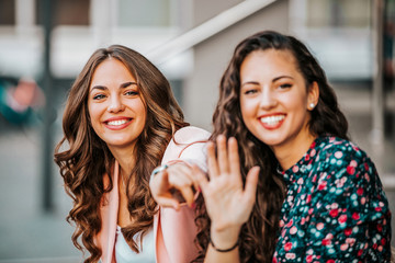 Shot of two attractive women sitting on the city street and waving at someone