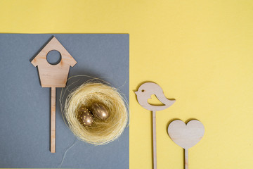 Holiday decoration. Easter egg gold colors. Yellow background, gray napkin. Wooden chicken, easter bunny on a stick.Flat lay, top view, trendy modern celebration style