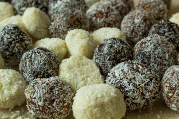 Coconut and chocolate balls covered with grated coconut on wooden plate