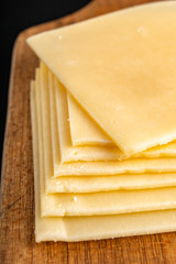 Slices of yellow cheese on a wooden board. Food from the market on the kitchen table.
