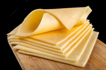 Slices of yellow cheese on a wooden board. Food from the market on the kitchen table.
