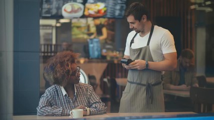 Woman using terminal for contactless payment with smartwatch in cafe - Powered by Adobe