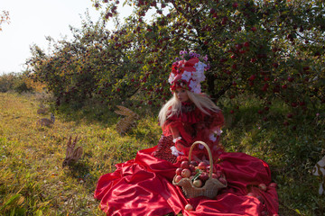 Fototapeta premium Sensual blond girl in fantasy red fairy tale stylization in apple park.
