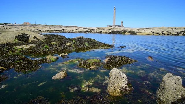 The lighthouse Phare de Gatteville and large rockpool on rocky shore at the Pointe de Barfleur, Normandy, France