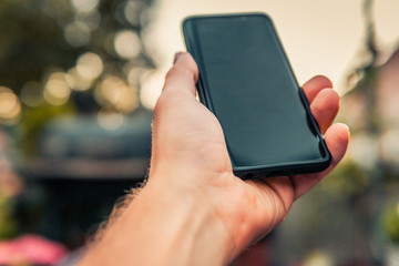 Male hand holding black smartphone with blurry background