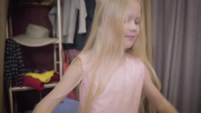 Camera moving up from feet of child putting on black elegant high heels to face of positive cute girl putting hands on hips and grimacing at camera. Lifestyle, fashion, beauty.