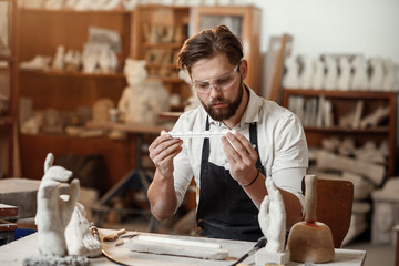 Concentrated sculptor with beard works in his workshop and looking at the ready gypsum decorative detail.