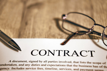 Contract sheet with glasses and pen on a wooden background