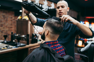 Good looking young adult man getting a hair and beard styling and dressing treatment by professional hairstylist.