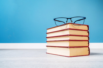 Pile stack of books on the floor or table in front of the blue wall with reading glasses on the top