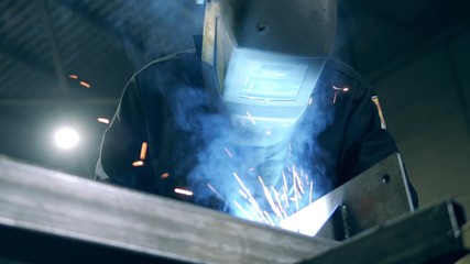 Close up of a welder in a protective helmet during work. Professional Heavy Industry Welder working at welding factory.