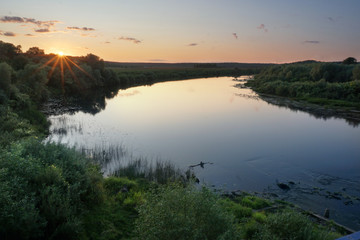 Landscape. Nature. Sunset over a river in a flat ground. Evening, soft lights, green meadows, calm water. The river makes a turn