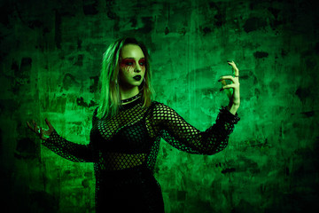 Zombie woman in halloween outfit posing with on a green background. Gorgeous girl in clothes celebrates the day of the dead. Halloween concept, witch costume, bright colors, steam punk.