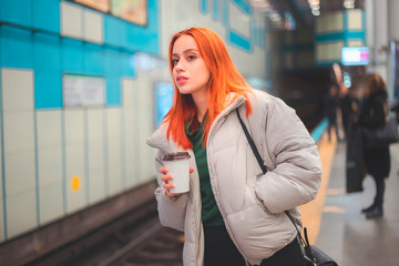 Attractive young redhead woman waiting and looking for a next train in a metro station