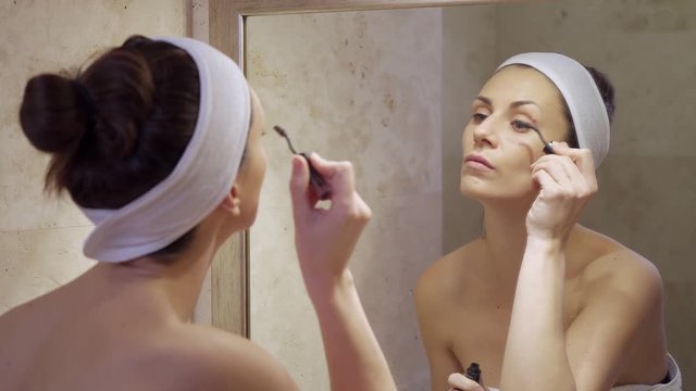 Beautiful young woman paints eyelashes in mirror in bathroom