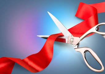 Scissors cutting the red ribbon on pastel background