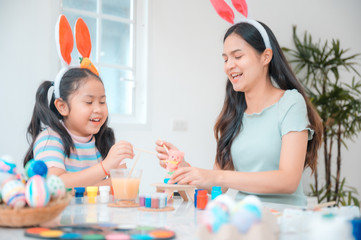 Attractive young woman with little cute girl are preparing for Easter celebration. Mom and daughter wearing bunny ears are having fun with Easter bunny while at home.