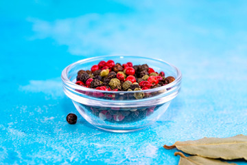 Multi-colored peppers in a glass bowl on a blue background. With place for text.
