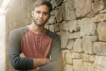 Obraz premium Gorgeous young man with optimistic expression alongside stone wall