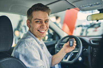 Delighted caucasian man hold a key from new car in showroom.