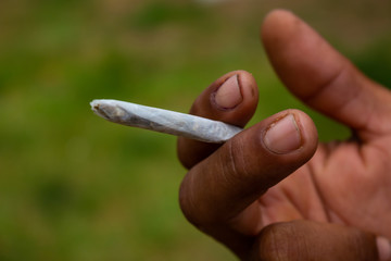Homemade cigarette held by the hand of a black man and dirty hands. Poverty and drug addiction concept. Marijuana in cigarette.