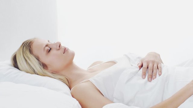 Young woman lying in the bed. Beautiful blond sleeping girl. Morning in the bedroom. Health and rest concept.