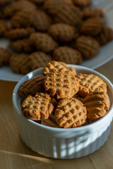 Very tasty peanut butter biscuits on bamboo wooden board in sunlight in white baking bowl, golden baked healthy cookies
