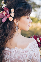 Naklejka premium Closeup portrait of a beautiful girl in a lace dress with a bouquet of red and burgundy flowers in her hands. A young woman walks outdoors, laughs and smiles. Girl with flowers in her hair.