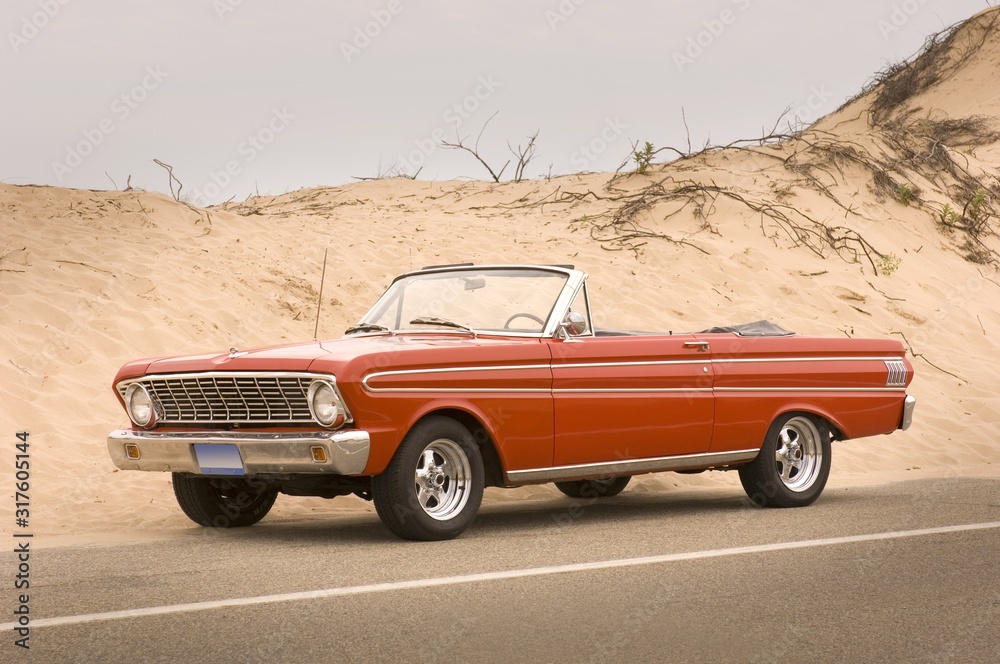 Sticker red convertible car on the road surrounded by hills covered in the sand