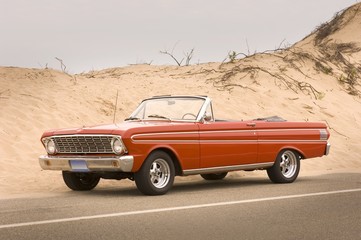 Red convertible car on the road surrounded by hills covered in the sand