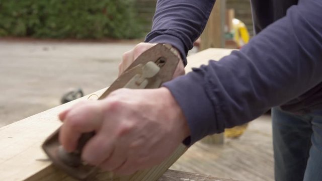 Man using an old wood planer on new beam for deck during a diy project at home during the day with wood shavings