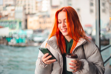 Attractive young redhead woman typing a message via her mobile phone in a ferryboat Istanbul and she is smiling