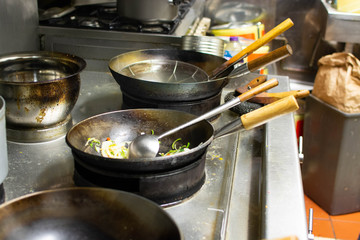 Chefs at work in a commercial kitchen. Male chef cooking using wok styled pans in a takeaway / restaurant setting