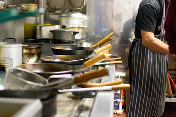 Chefs at work in a commercial kitchen. Male chef cooking using wok styled pans in a takeaway / restaurant setting