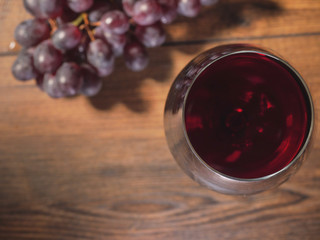 Glass of red wine in focus, cluster of fresh red grapes on a wooden table out of focus, top view.