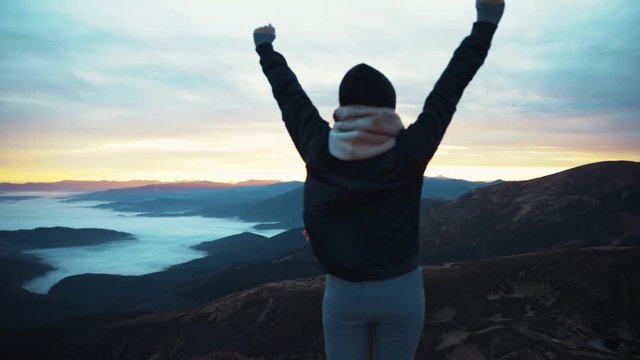 Back view of woman standing raised arms of the mountain in Norway at sunset no people around adventure pure nature enjoying the landscape slow motion sky clouds on the hill