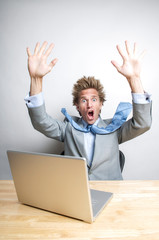 Shocked businessman falling back from his laptop computer working at his office desk 