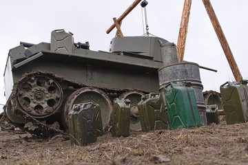 Soviet tank of the second world war during the repair with the tower raised on the winch. Canisters and barrels of fuel and oil in the foreground.