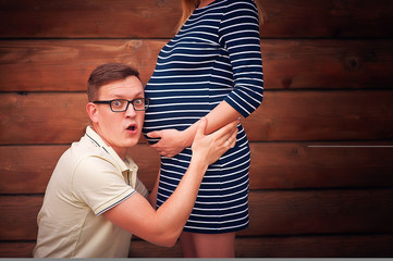 Handsome man is listening to his beautiful pregnant wife's tummy and smiling