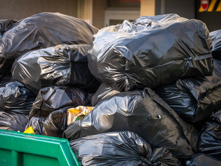 A lot of black plastic bags of garbage are dumped in a dumpster