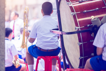 Fototapeta premium Selective focus to back of the musician that hand is holding the trumpet with blurry big drum, ready to play in the orchestra band. Thai student.