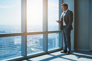 Mature business executive texting alongside large windows with sunflare