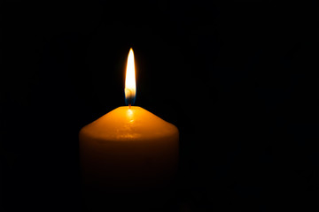 Single burning wax candle flame isolated on the black background