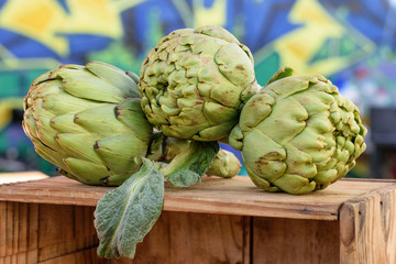 Obraz premium Group of fresh green artichokes on the wooden box for saling at the market place.