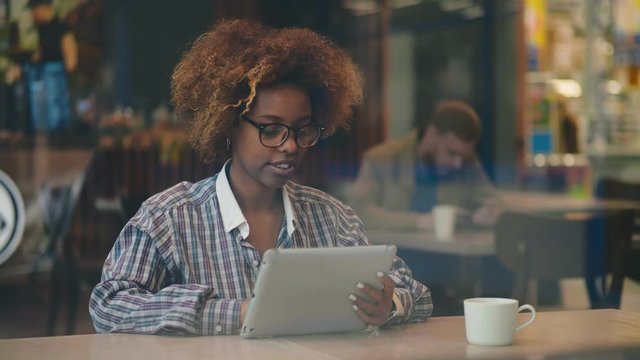 African female freelancer working on tablet sitting in cafe