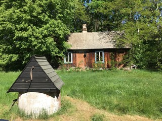 Piękny stary rozpadający się dom na Mazowszu w Polsce, na pierwszym planie stara studnia - wszystko zarośnięte zielenią