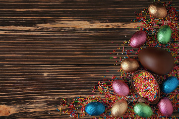 Sweet chocolate eggs in shiny colored foil wrapper around on dark wooden table. Easter flat lay composition.