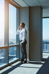 Confident businessman in office space on top floor using mobile phone